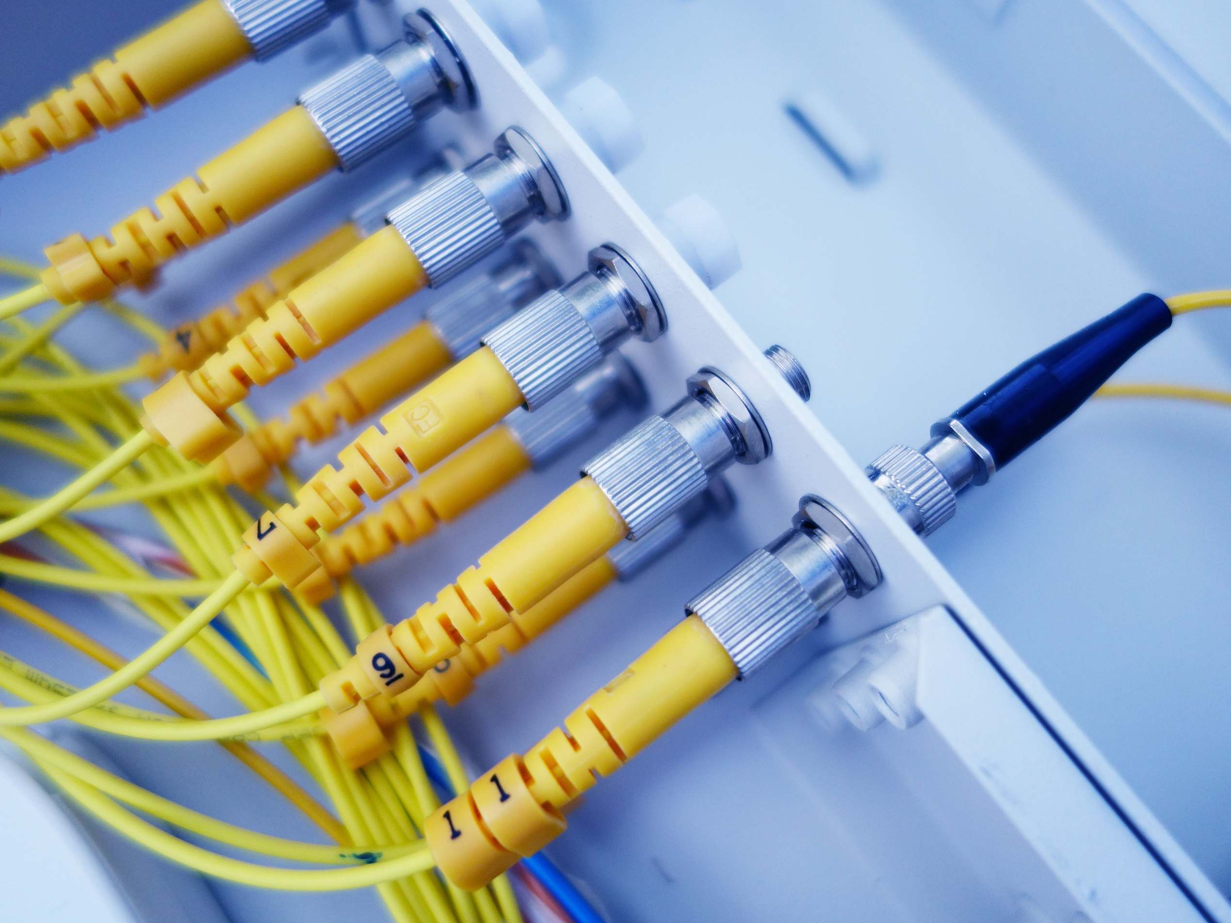 Rows of server racks in a data hall, close-up of yellow fiber optic cables in a network server