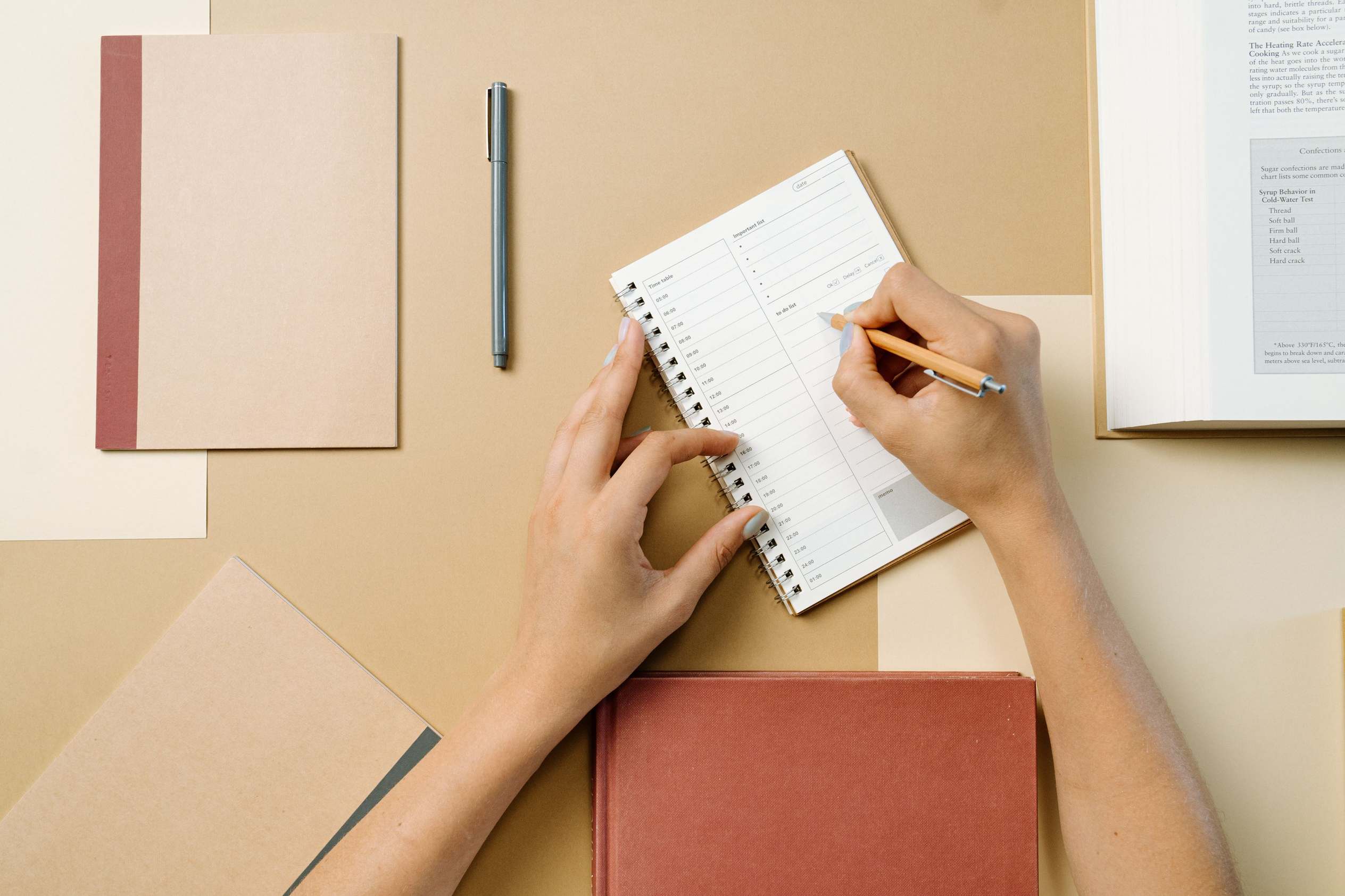 Overhead flat lay of notebook sketches and pens, hands writing in a spiral notebook on a desk